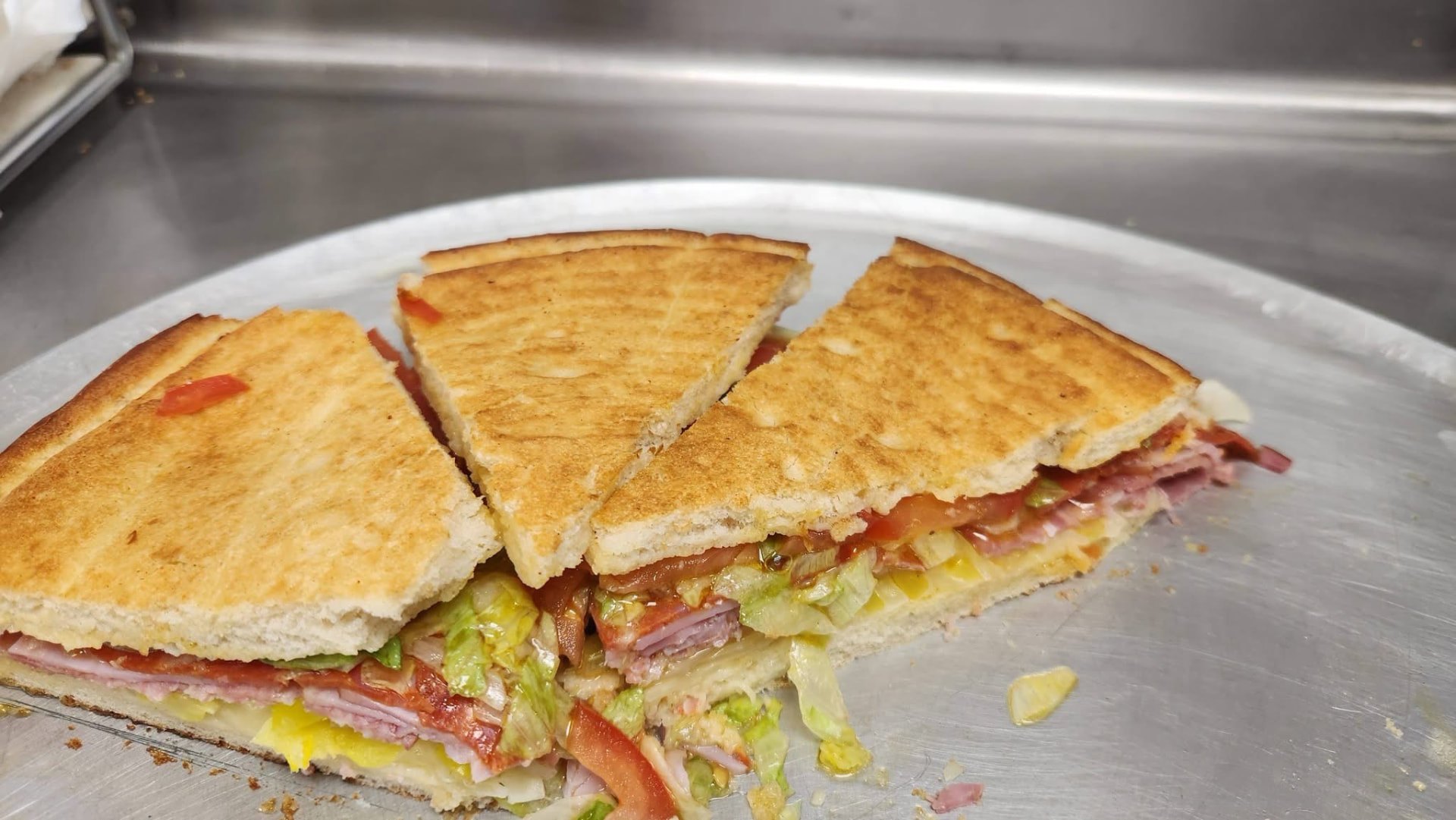 Flatbread layered with deli meats, lettuce, tomato and banana peppers, cut into wedges