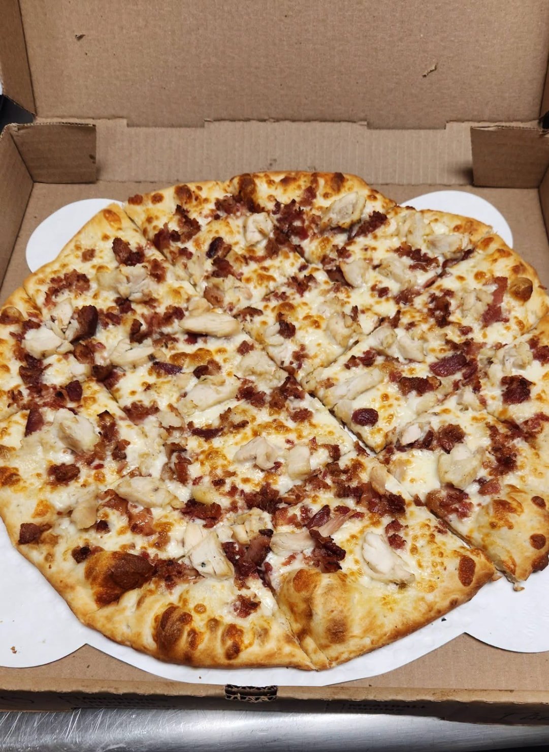 Chicken and bacon pizza with a white sauce base, sliced in an open takeout box