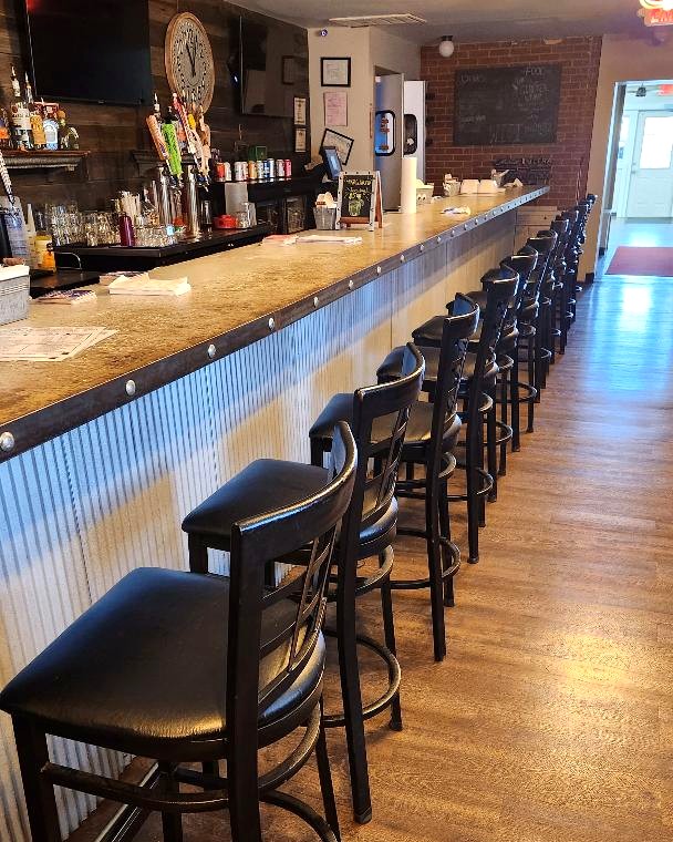 The long bar counter at Gibeye’s Pizza with black bar stools, tap handles, a wall clock and TVs down the aisle