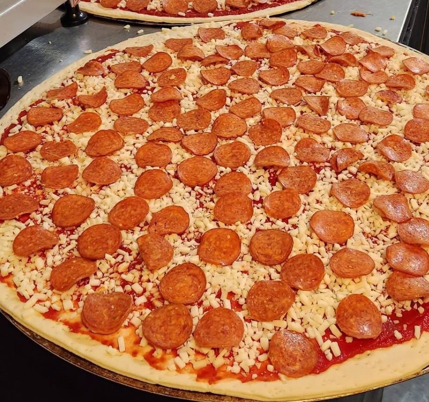 Pepperoni pizzas assembled on the prep counter, ready for the oven