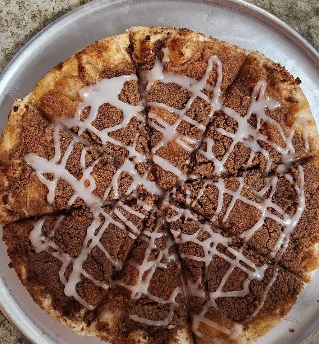Dessert pizza topped with cinnamon sugar and a white icing drizzle, sliced on a round pan